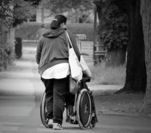 žena před sebou v parku tlačí člověka na vozíku